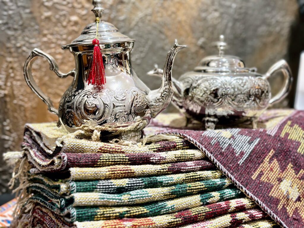 Théières en cuivre blanc gravées à la main du Maroc et pile de tapis faits main en Turquie chez Nakshedil Boutique à Remich.